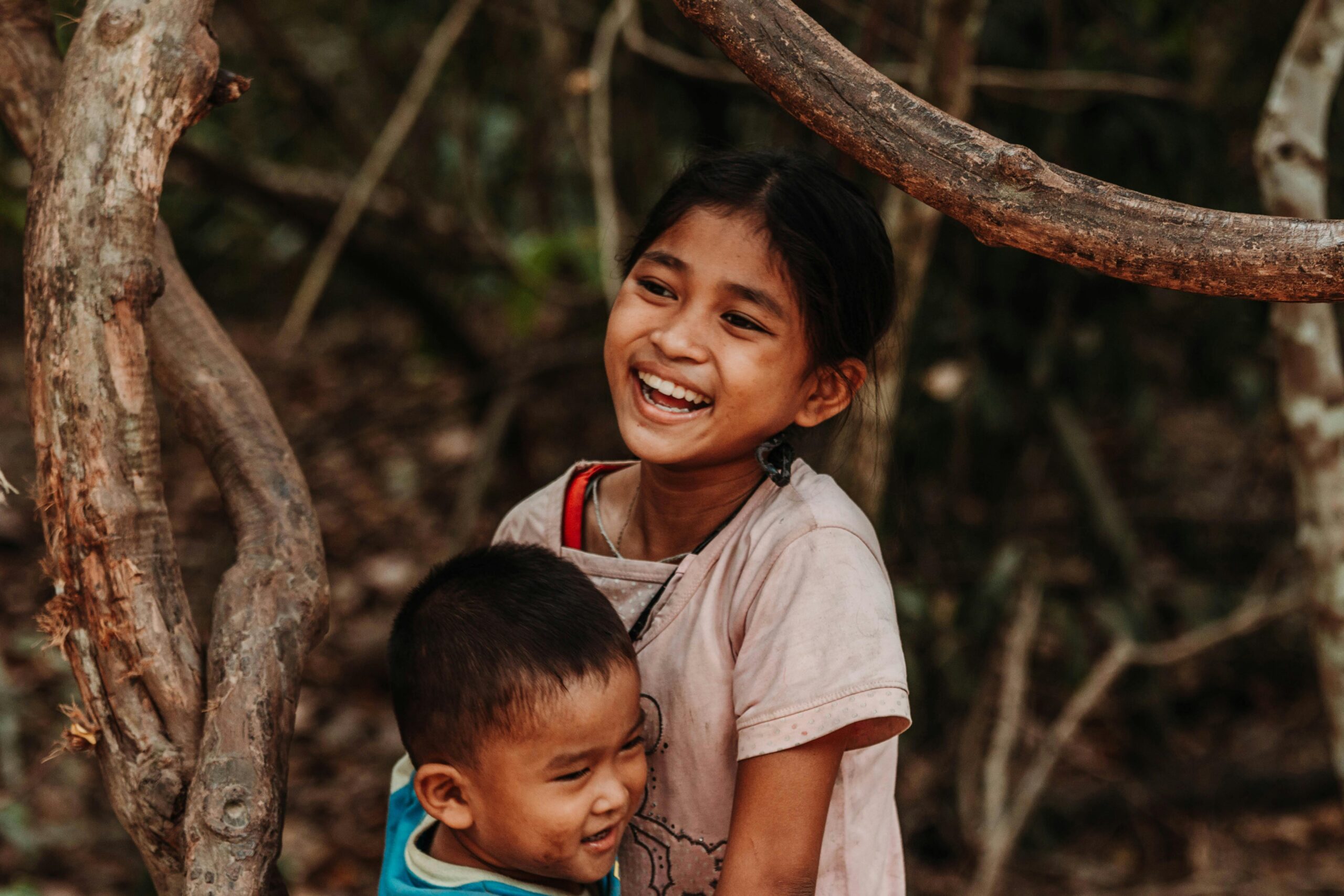 Happy siblings laughing together while playing outside among trees.