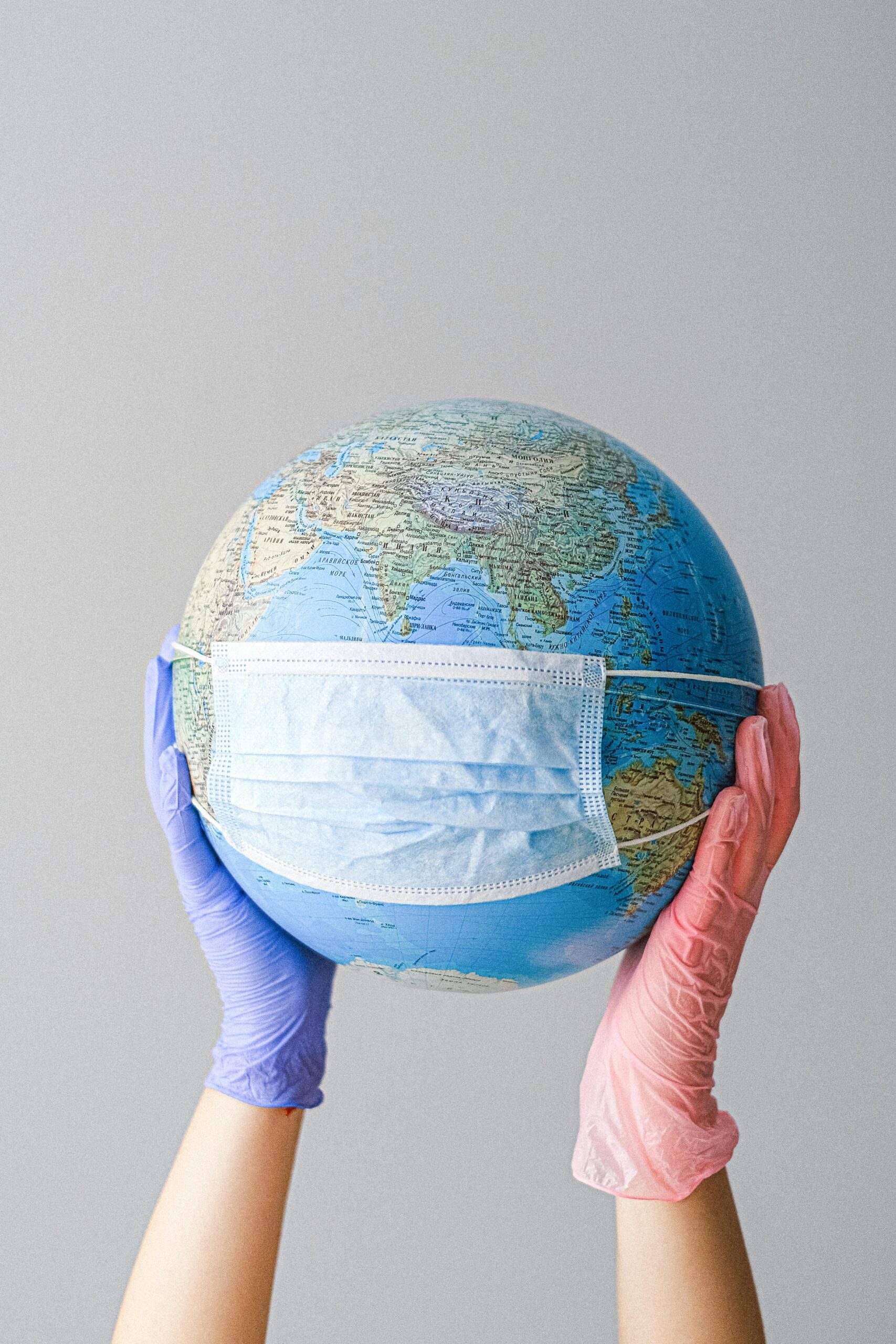Hands in gloves holding a globe with a mask, symbolizing global health and pandemic protection.